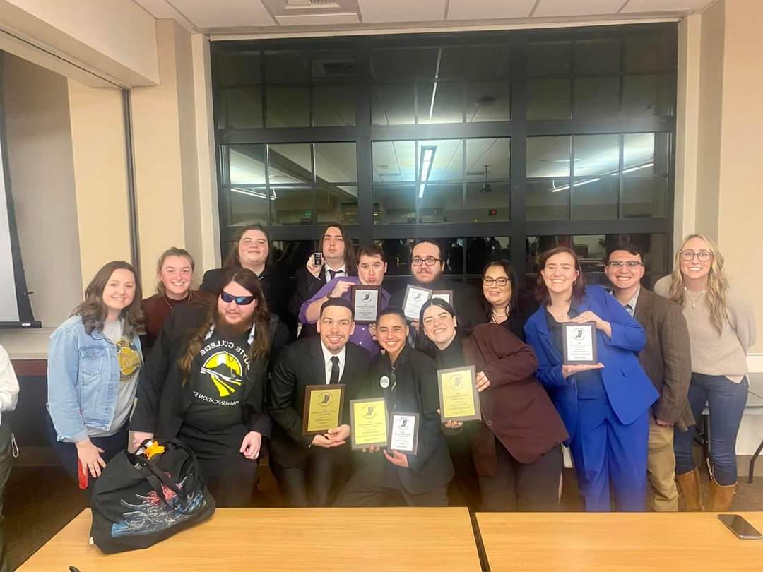 a group photo of the speech and debate team holding up multiple awards.